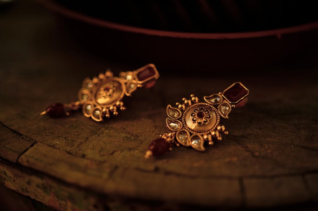 Close-up of intricate gold earrings with gemstones laid on a rustic wooden surface.