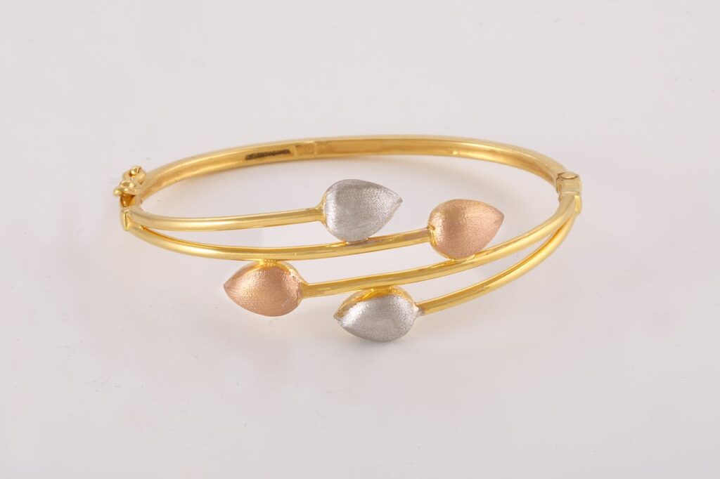 Stylish gold bangle featuring a unique leaf design in silver and rose gold accents.