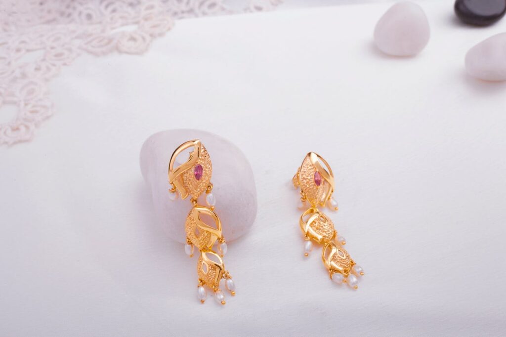 Gold earrings with gemstones and pearls displayed on a white marble surface.